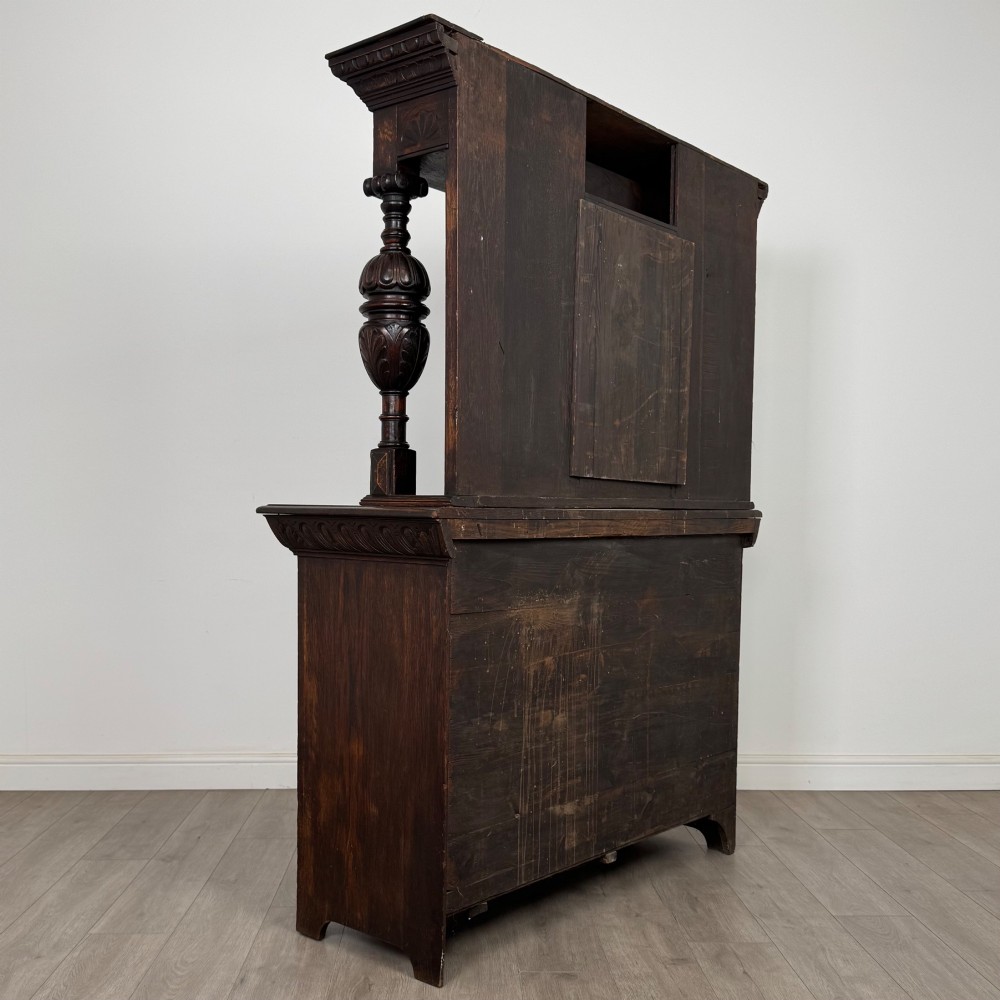 A 19th-century dark carved oak Victorian sideboard featuring an upper mirrored shelf section supported by turned bulbous pilasters above two carved drawers and cupboard doors with rosette reliefs. View V