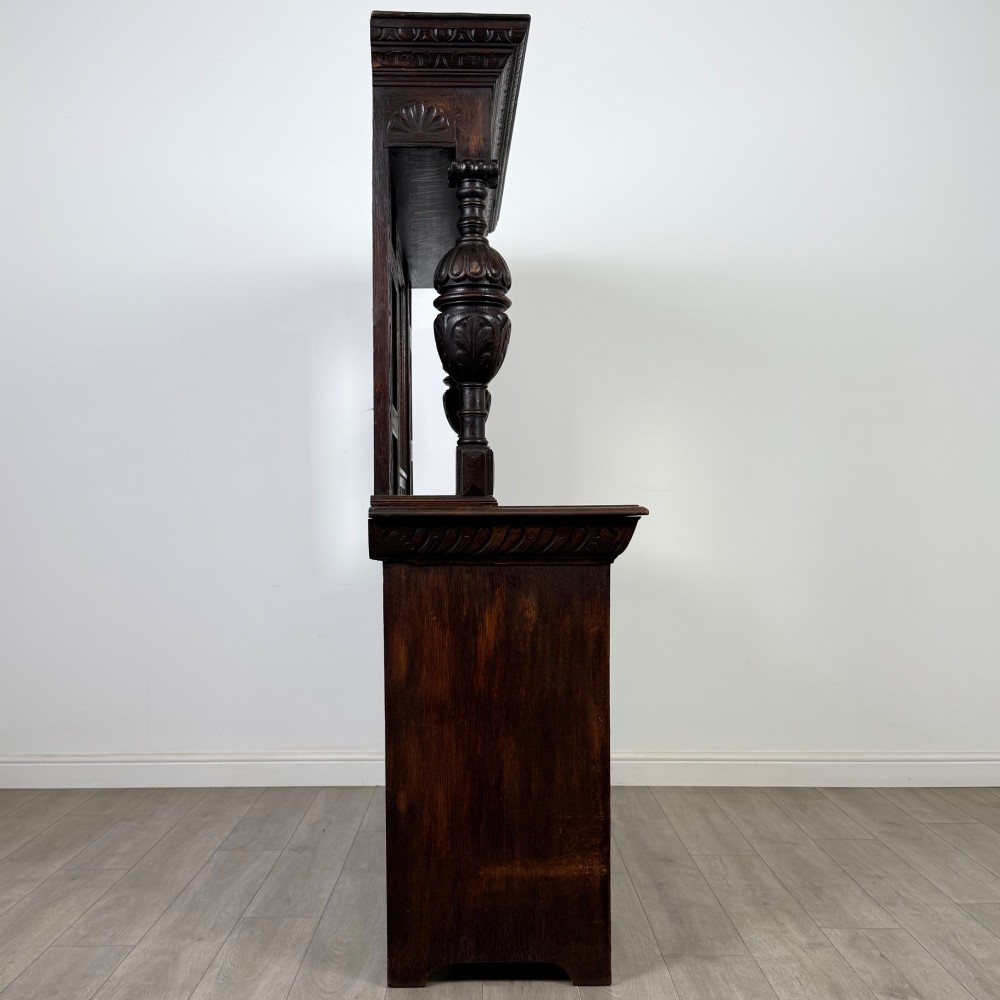 A 19th-century dark carved oak Victorian sideboard featuring an upper mirrored shelf section supported by turned bulbous pilasters above two carved drawers and cupboard doors with rosette reliefs. View VIII