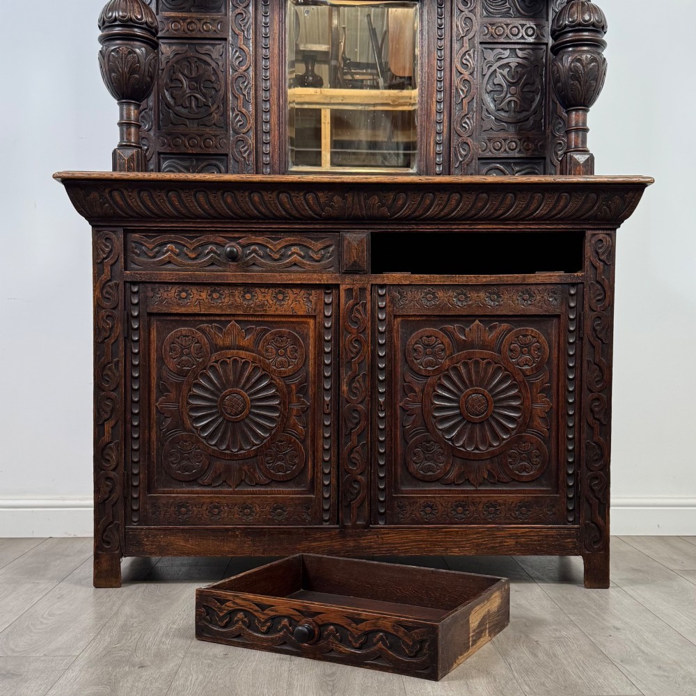 A 19th-century dark carved oak Victorian sideboard featuring an upper mirrored shelf section supported by turned bulbous pilasters above two carved drawers and cupboard doors with rosette reliefs. View XI