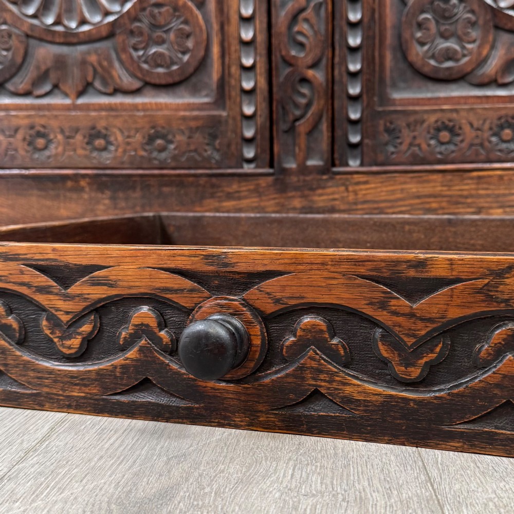 A 19th-century dark carved oak Victorian sideboard featuring an upper mirrored shelf section supported by turned bulbous pilasters above two carved drawers and cupboard doors with rosette reliefs. View XII