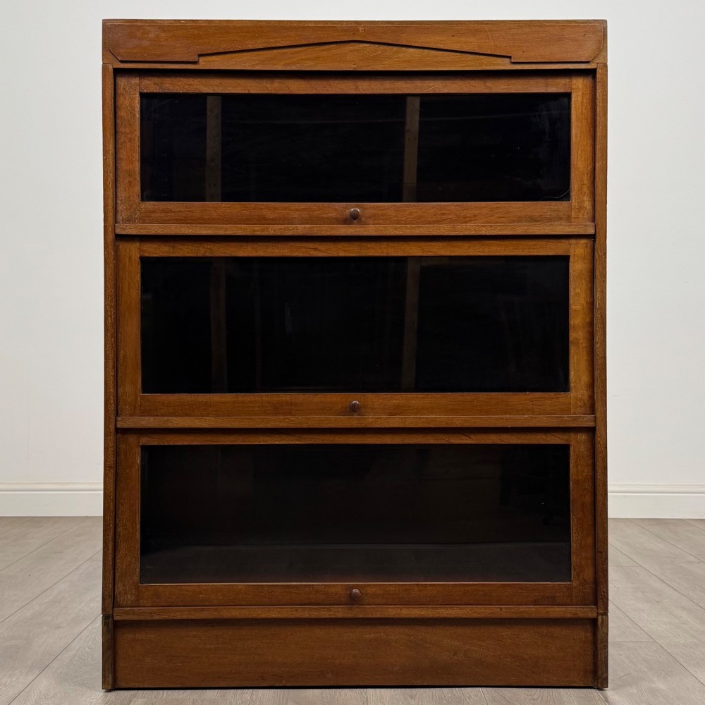 A three-tier mahogany sectional bookcase featuring lift-up glazed doors with small wooden knobs.