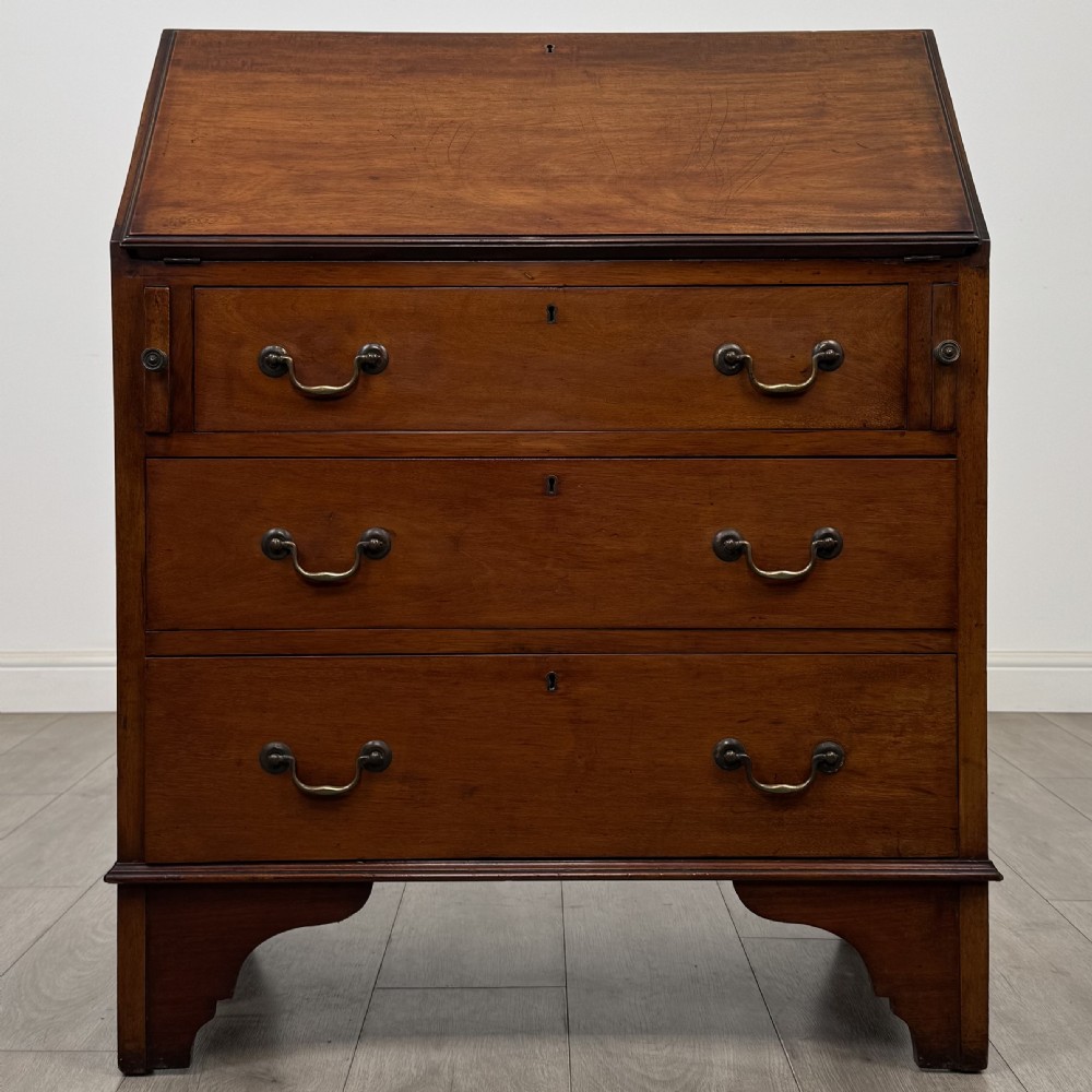 An Edwardian mahogany writing bureau featuring a slant front top, three long drawers with brass drop handles, and shaped bracket feet.