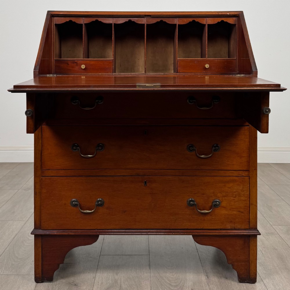 An Edwardian mahogany writing bureau featuring a slant front top, three long drawers with brass drop handles, and shaped bracket feet. View II