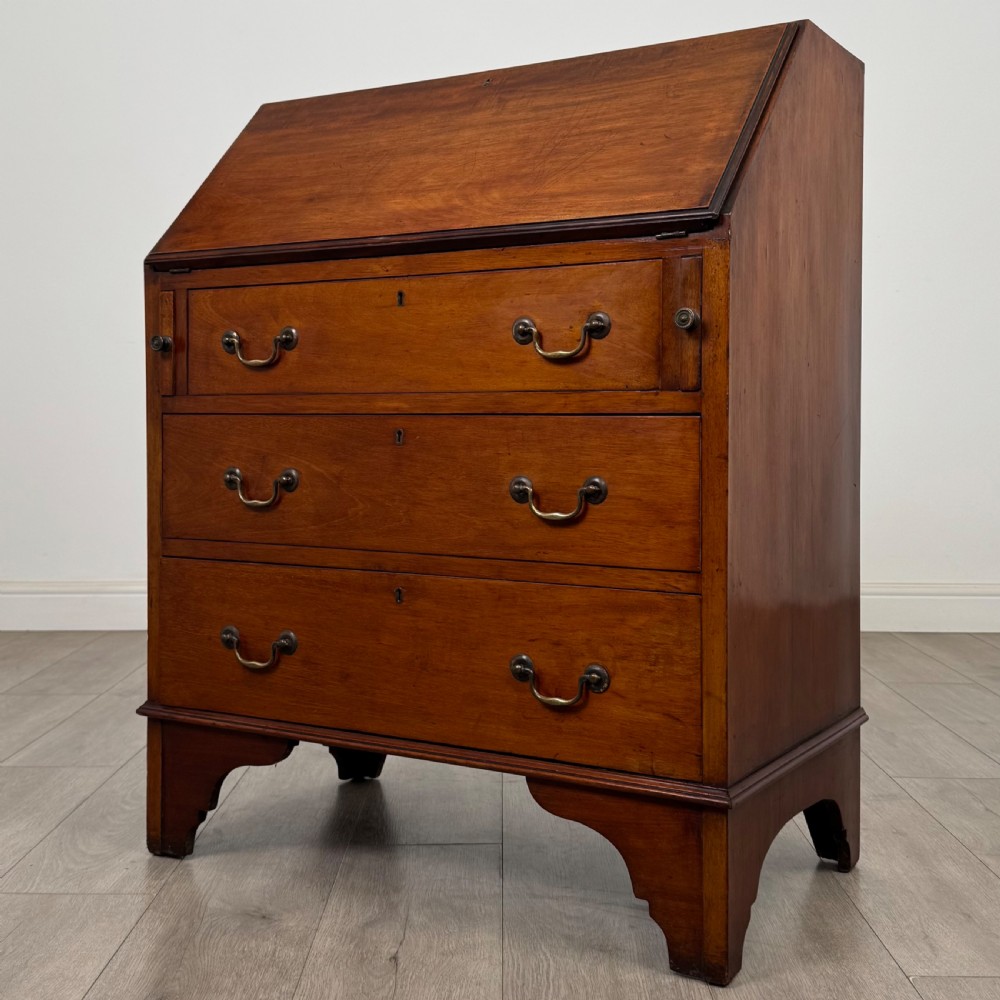 An Edwardian mahogany writing bureau featuring a slant front top, three long drawers with brass drop handles, and shaped bracket feet. View III