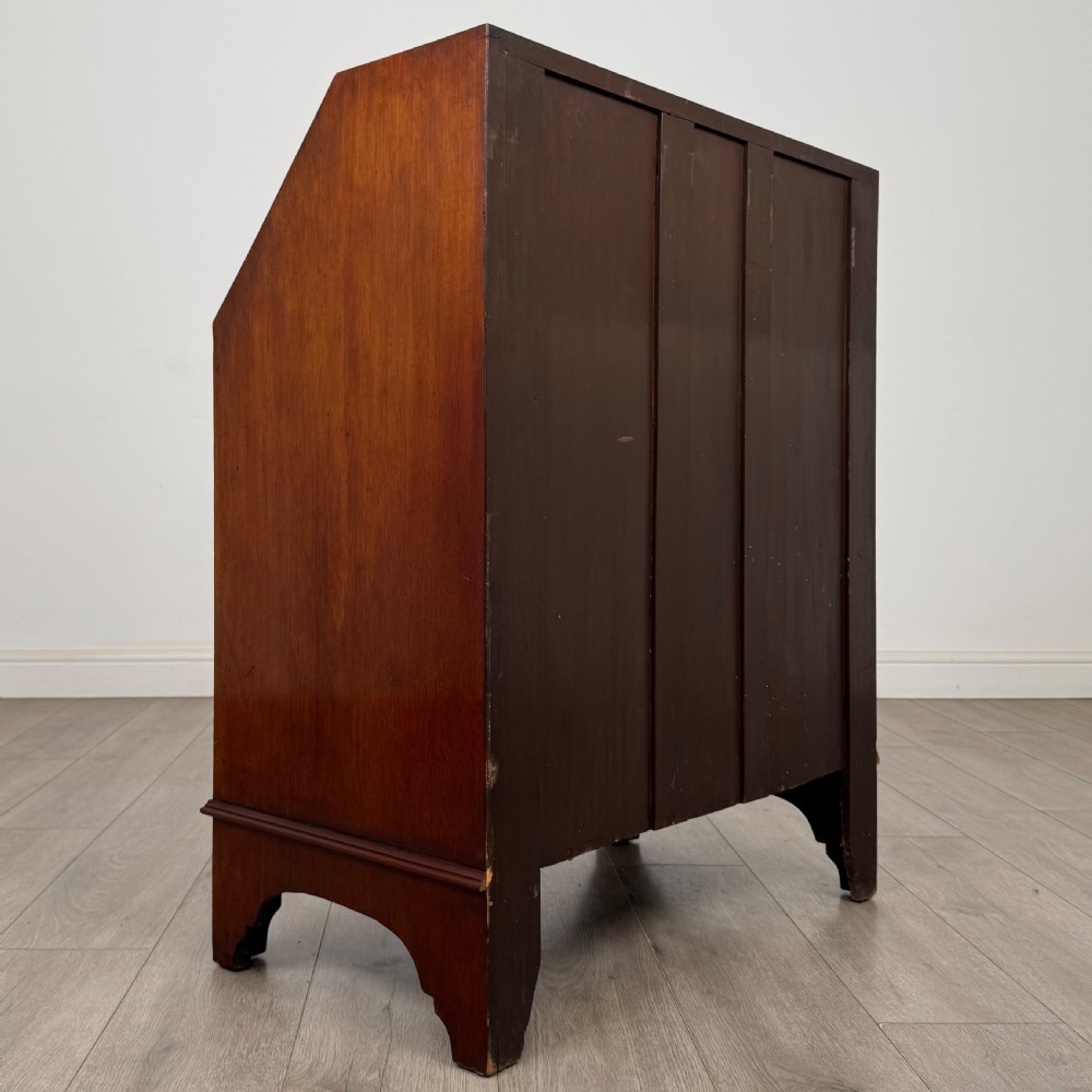 An Edwardian mahogany writing bureau featuring a slant front top, three long drawers with brass drop handles, and shaped bracket feet. View V