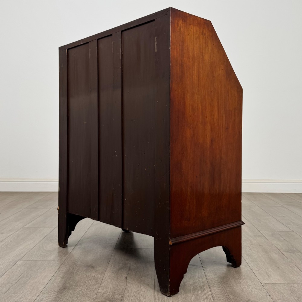 An Edwardian mahogany writing bureau featuring a slant front top, three long drawers with brass drop handles, and shaped bracket feet. View VII