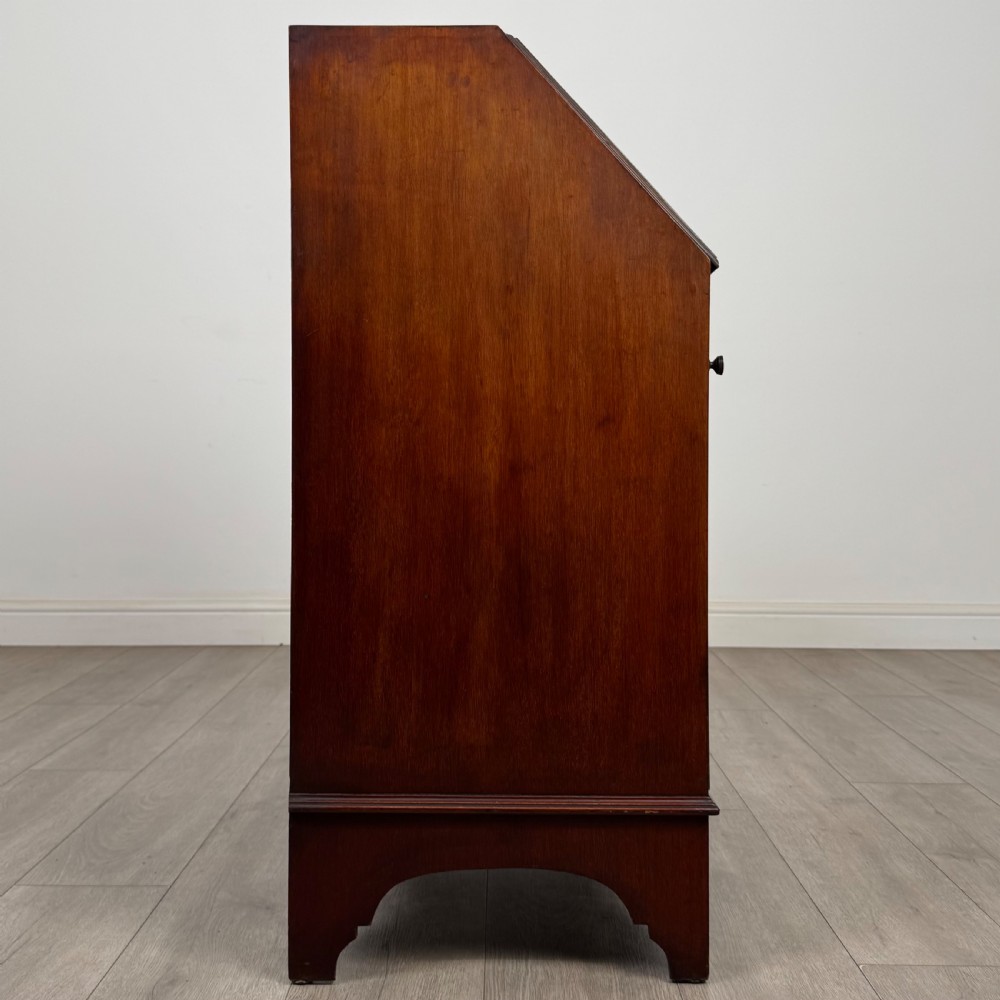 An Edwardian mahogany writing bureau featuring a slant front top, three long drawers with brass drop handles, and shaped bracket feet. View VIII