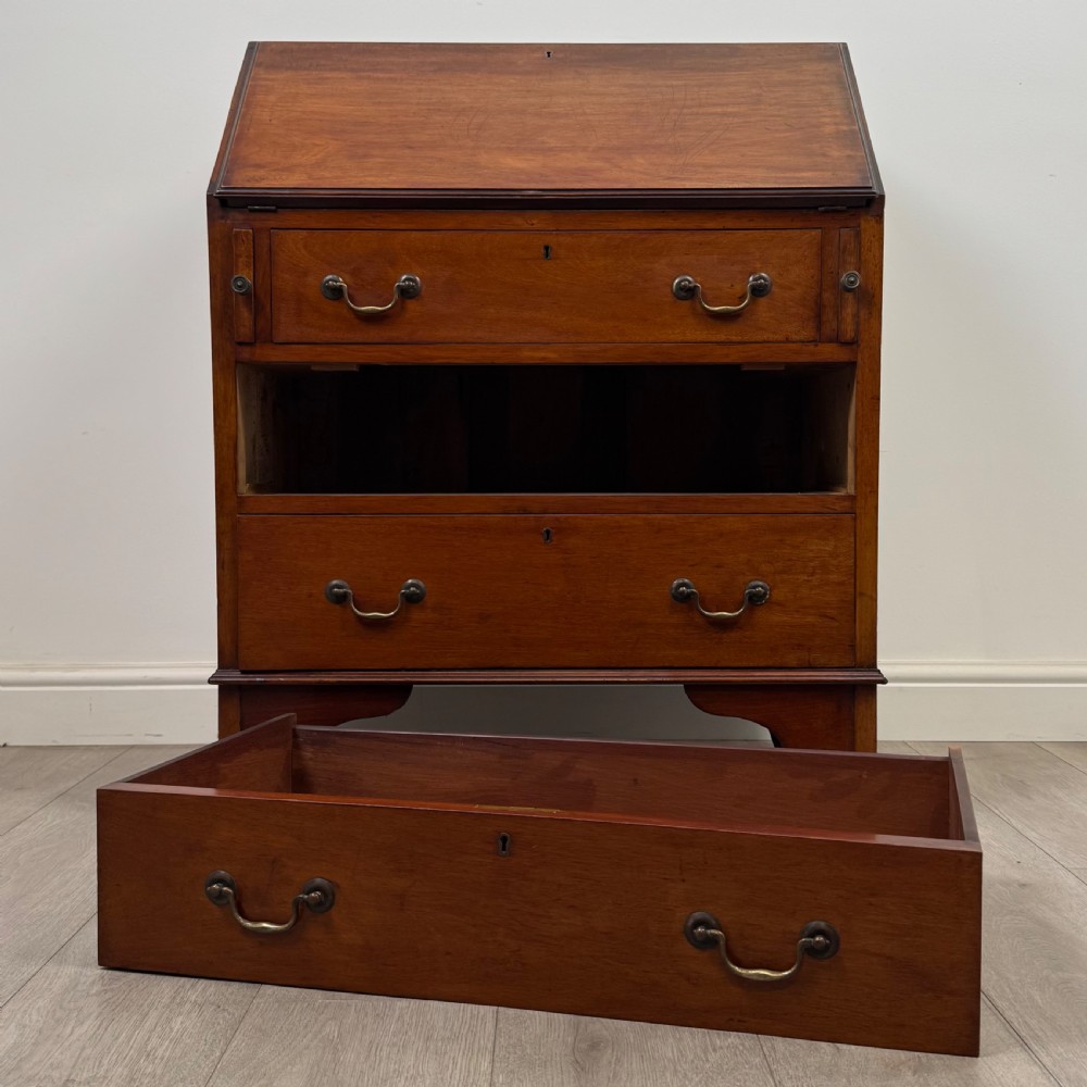 An Edwardian mahogany writing bureau featuring a slant front top, three long drawers with brass drop handles, and shaped bracket feet. View XII