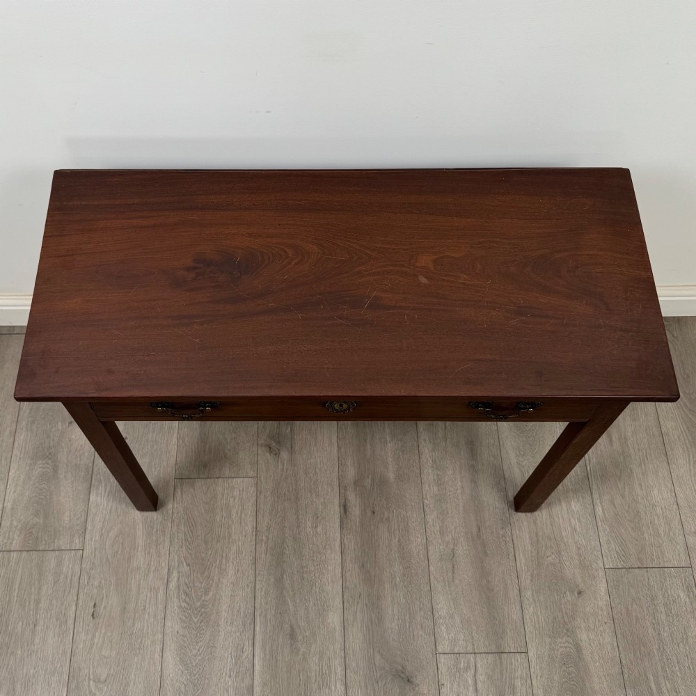 An 18th-century Georgian mahogany writing table featuring a rectangular top, a single wide frieze drawer with brass handles and central escutcheon, supported by straight square legs. View X