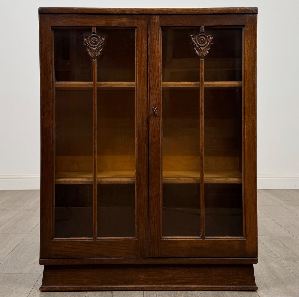 An Edwardian dark oak display cabinet with two glazed doors featuring vertical glazing bars topped with carved floral details.