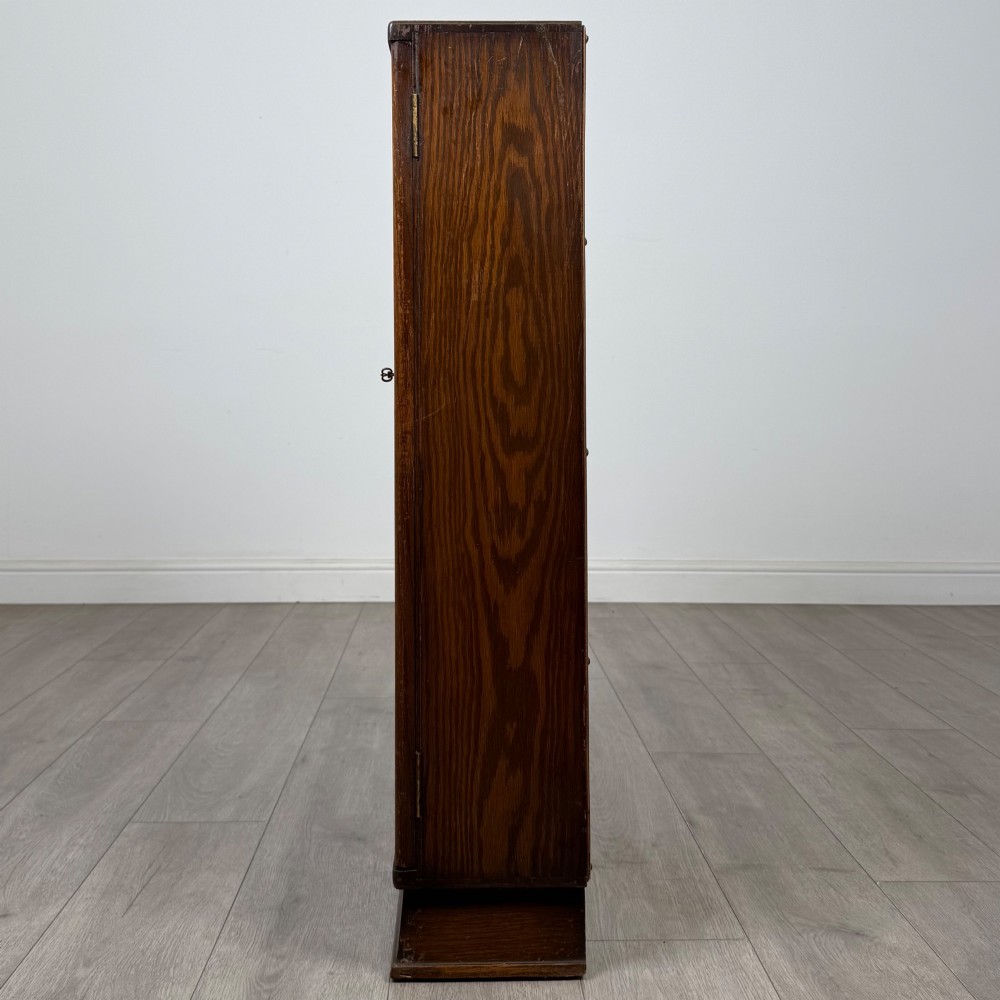 An Edwardian dark oak display cabinet with two glazed doors featuring vertical glazing bars topped with carved floral details. View IV