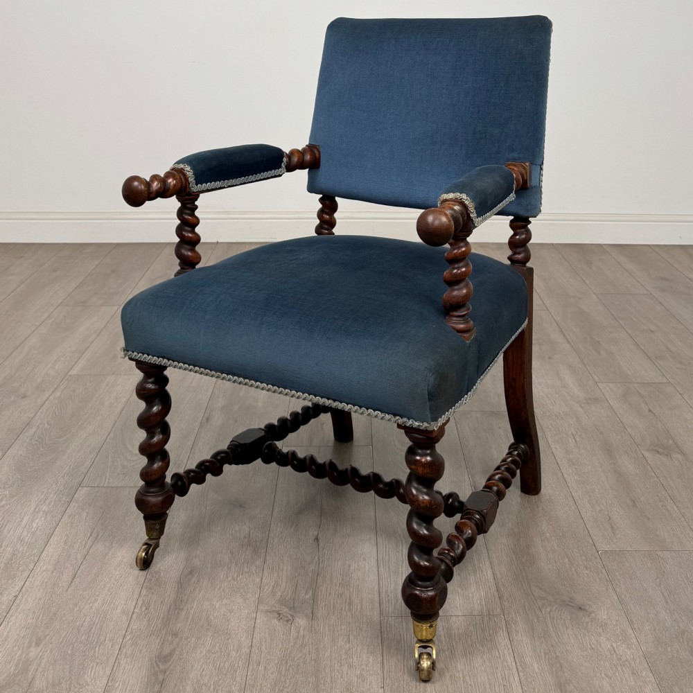 A nineteenth-century dark oak armchair featuring barley twist legs and stretchers, blue fabric upholstery, and brass front castors.