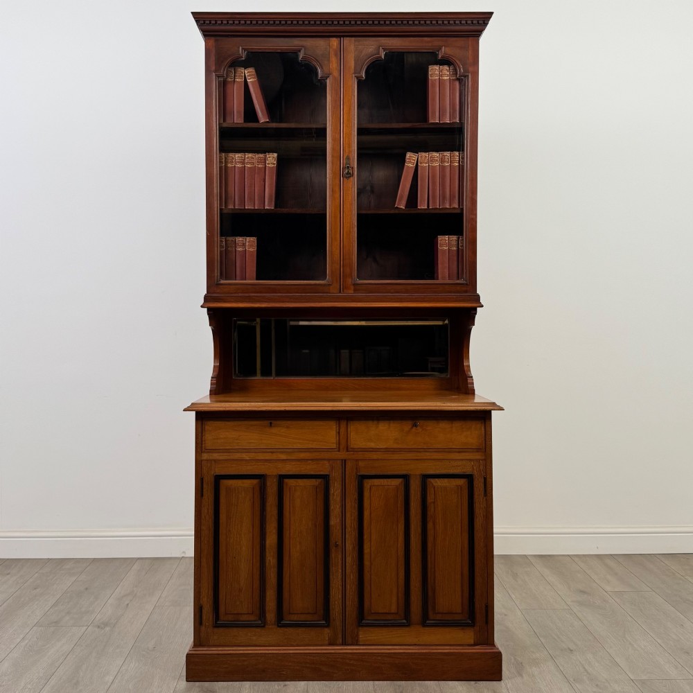 An Edwardian walnut bookcase featuring a two-door glazed upper section with arched frames, a central mirrored niche, and a base cabinet with drawers and panelled doors.