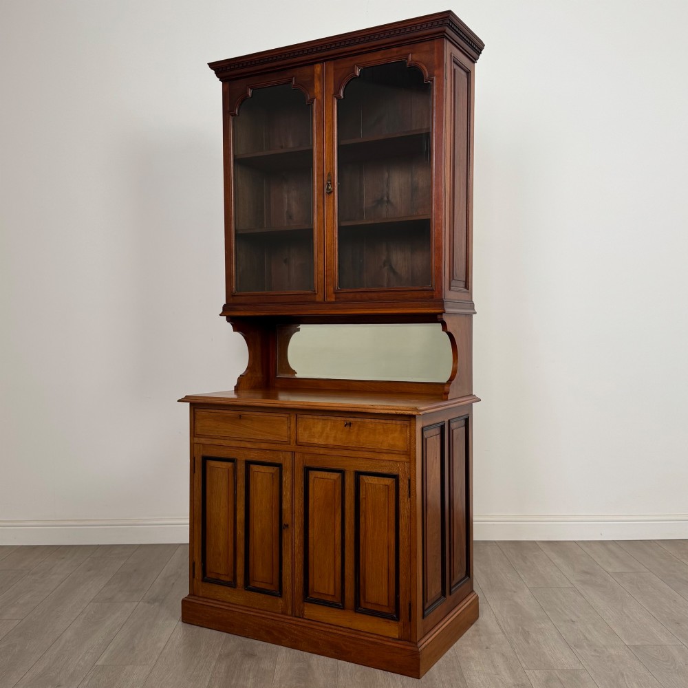 An Edwardian walnut bookcase featuring a two-door glazed upper section with arched frames, a central mirrored niche, and a base cabinet with drawers and panelled doors. View IV
