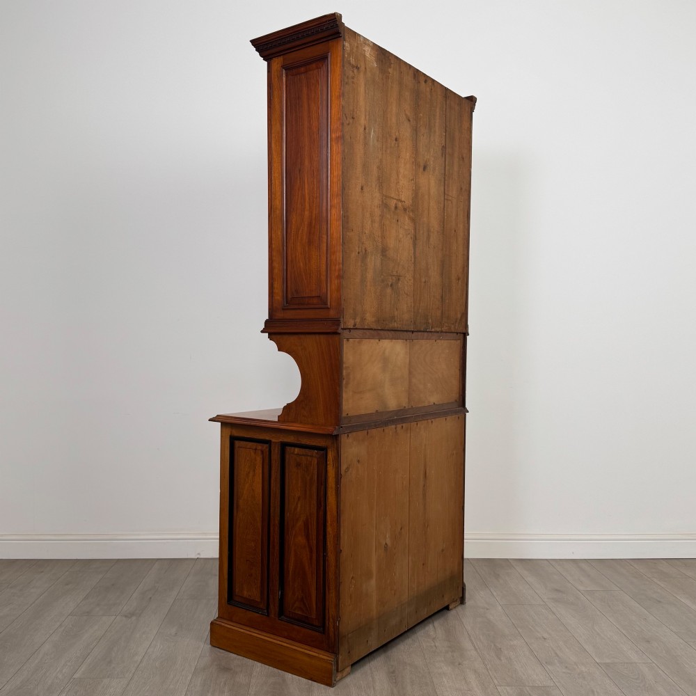 An Edwardian walnut bookcase featuring a two-door glazed upper section with arched frames, a central mirrored niche, and a base cabinet with drawers and panelled doors. View VI