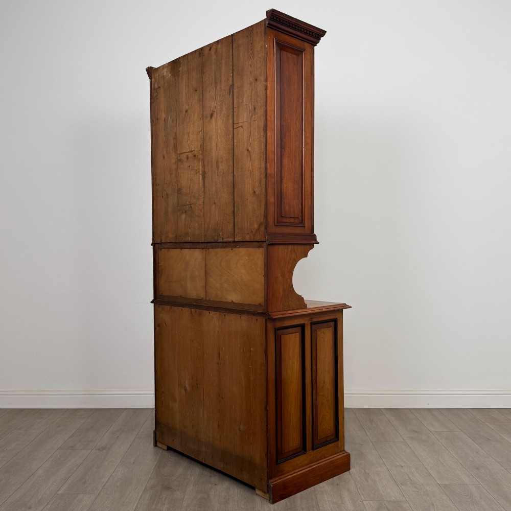 An Edwardian walnut bookcase featuring a two-door glazed upper section with arched frames, a central mirrored niche, and a base cabinet with drawers and panelled doors. View VIII