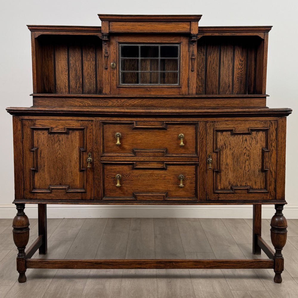 A 20th-century Jacobean style dark oak sideboard with a central leaded glass cupboard, geometric moulded drawers and doors, turned legs, and stretchers.