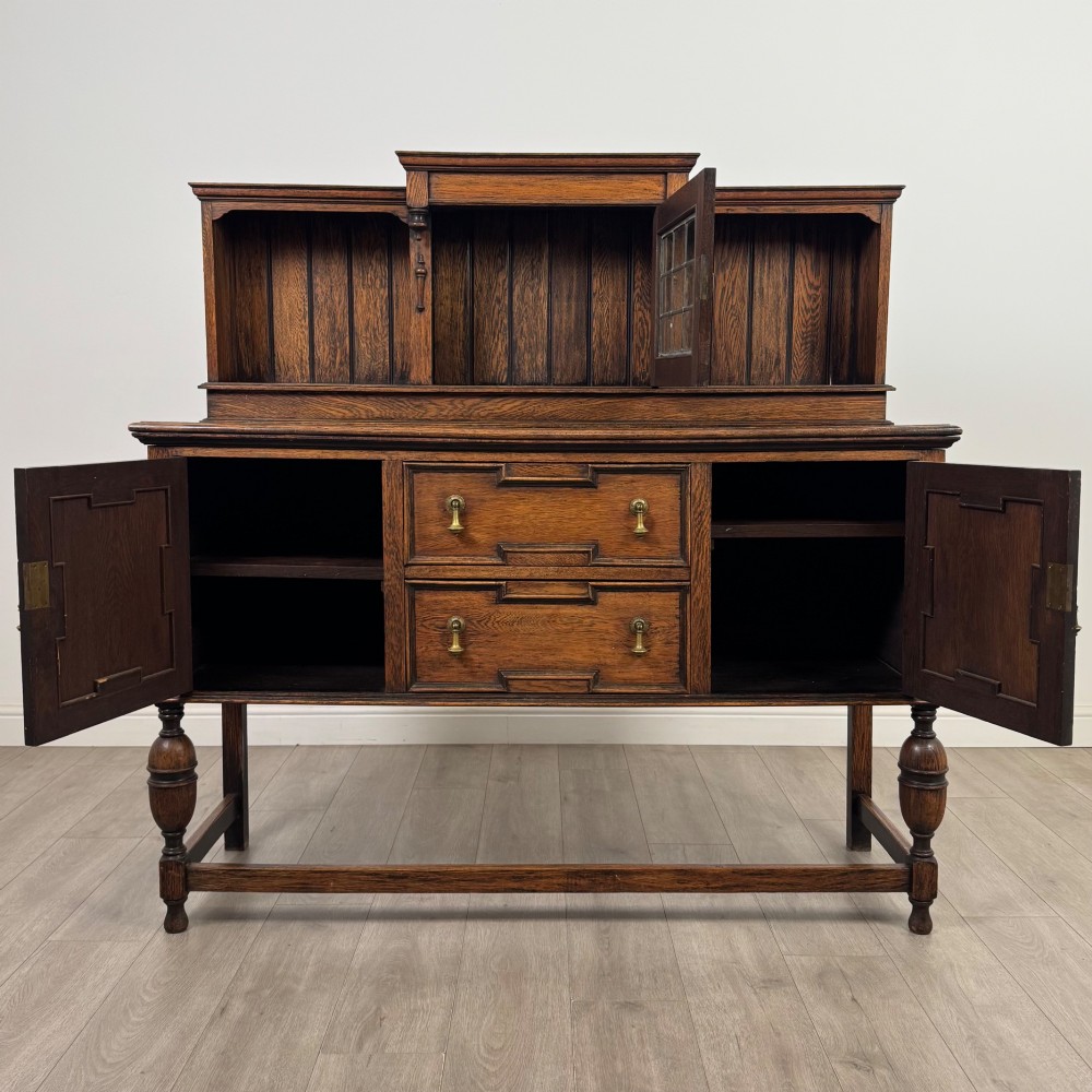 A 20th-century Jacobean style dark oak sideboard with a central leaded glass cupboard, geometric moulded drawers and doors, turned legs, and stretchers. View II