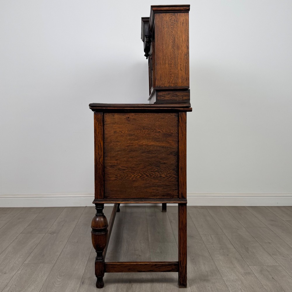 A 20th-century Jacobean style dark oak sideboard with a central leaded glass cupboard, geometric moulded drawers and doors, turned legs, and stretchers. View IV