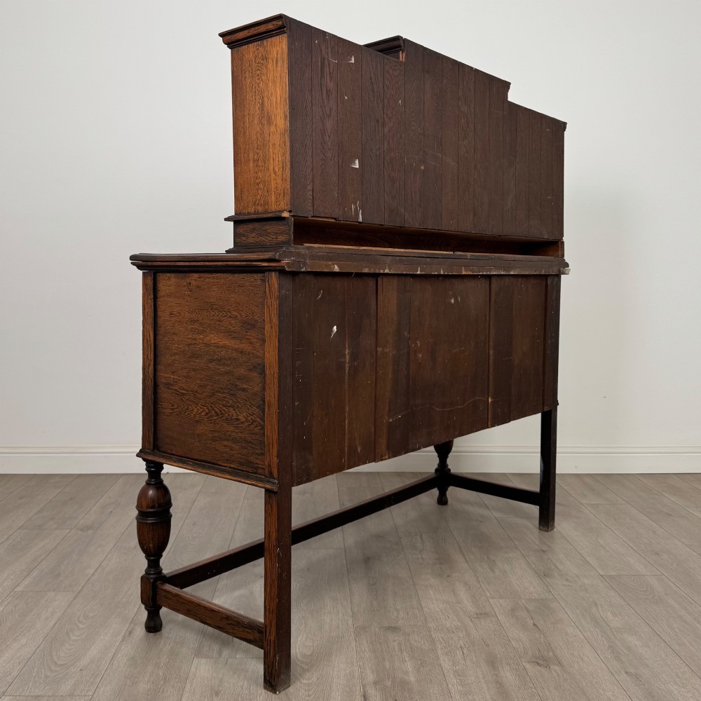 A 20th-century Jacobean style dark oak sideboard with a central leaded glass cupboard, geometric moulded drawers and doors, turned legs, and stretchers. View V