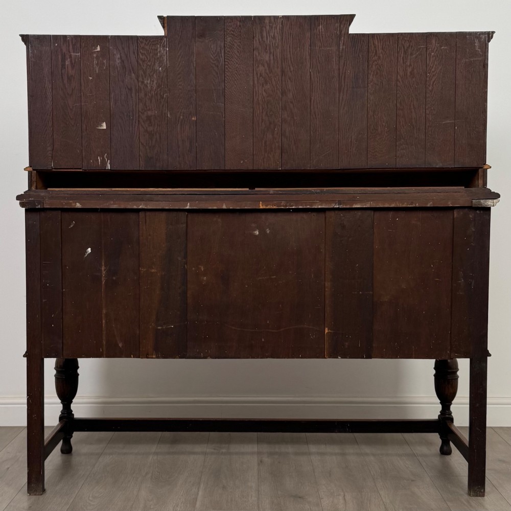 A 20th-century Jacobean style dark oak sideboard with a central leaded glass cupboard, geometric moulded drawers and doors, turned legs, and stretchers. View VI
