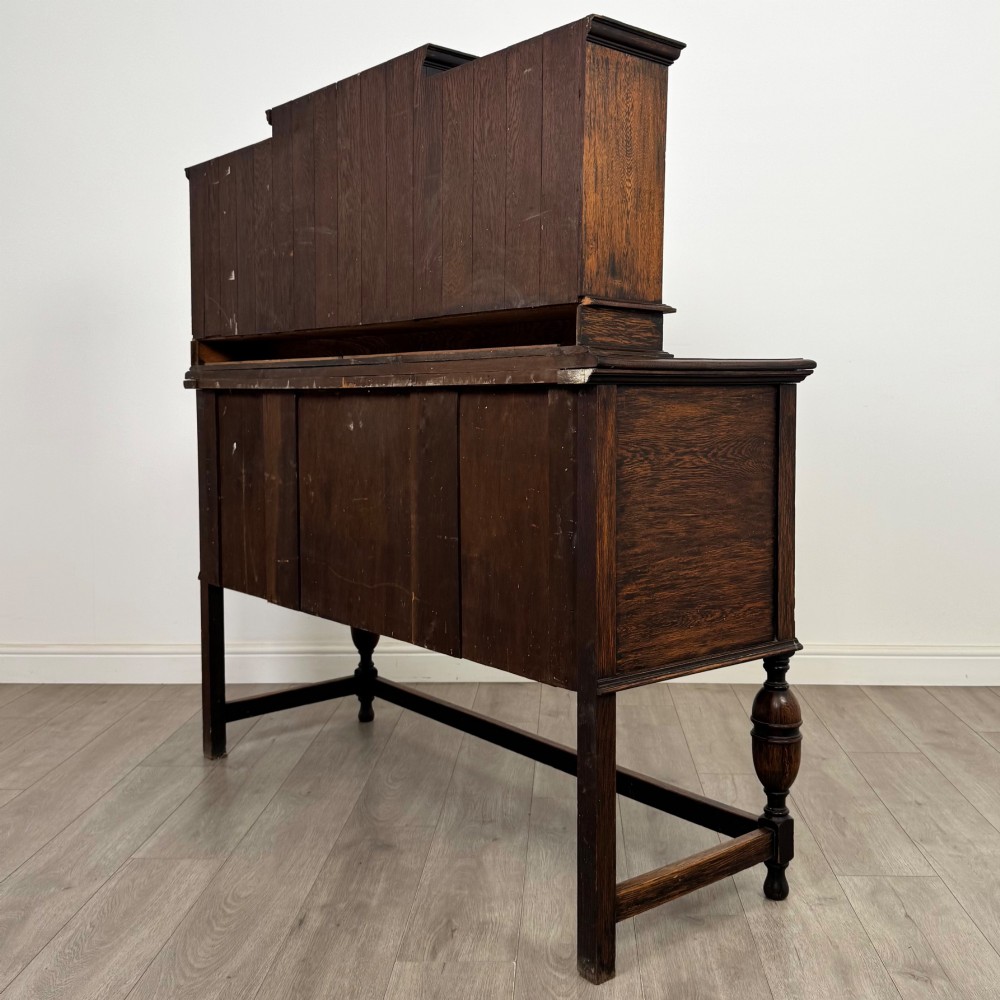 A 20th-century Jacobean style dark oak sideboard with a central leaded glass cupboard, geometric moulded drawers and doors, turned legs, and stretchers. View VII
