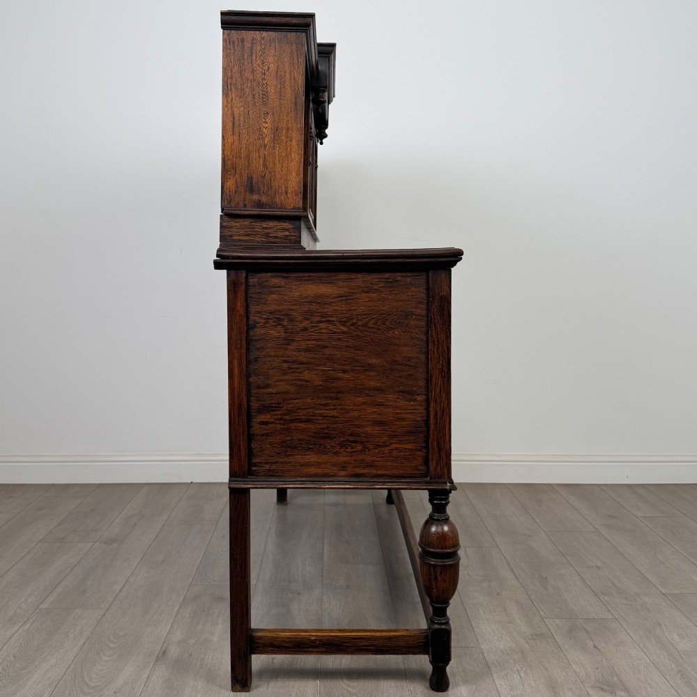 A 20th-century Jacobean style dark oak sideboard with a central leaded glass cupboard, geometric moulded drawers and doors, turned legs, and stretchers. View VIII