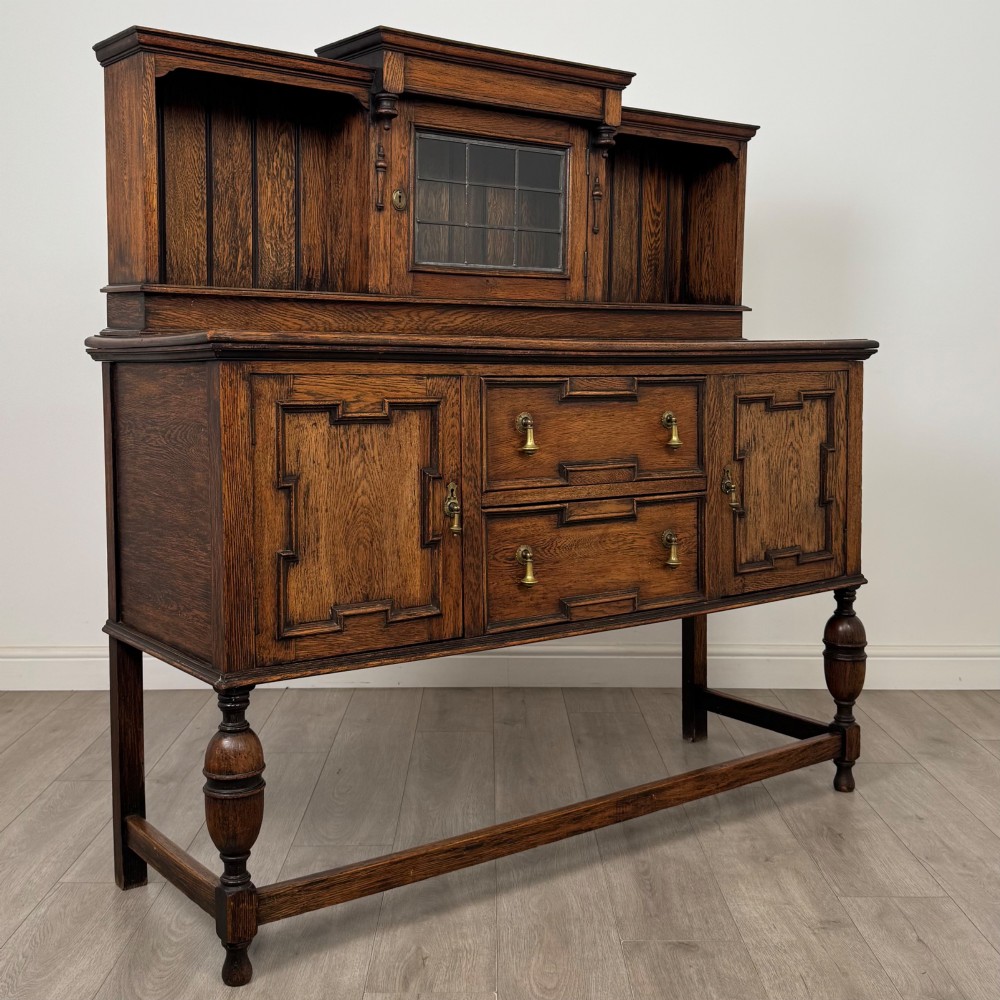 A 20th-century Jacobean style dark oak sideboard with a central leaded glass cupboard, geometric moulded drawers and doors, turned legs, and stretchers. View IX