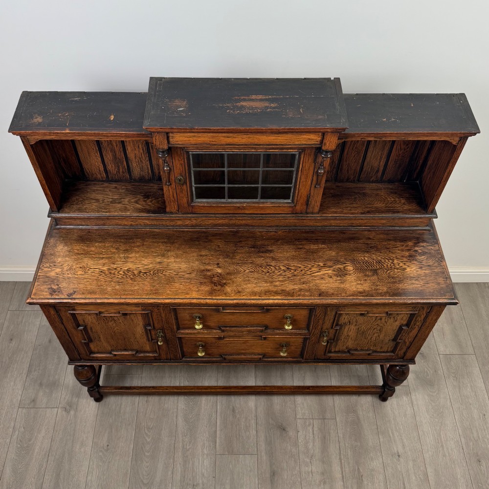 A 20th-century Jacobean style dark oak sideboard with a central leaded glass cupboard, geometric moulded drawers and doors, turned legs, and stretchers. View X