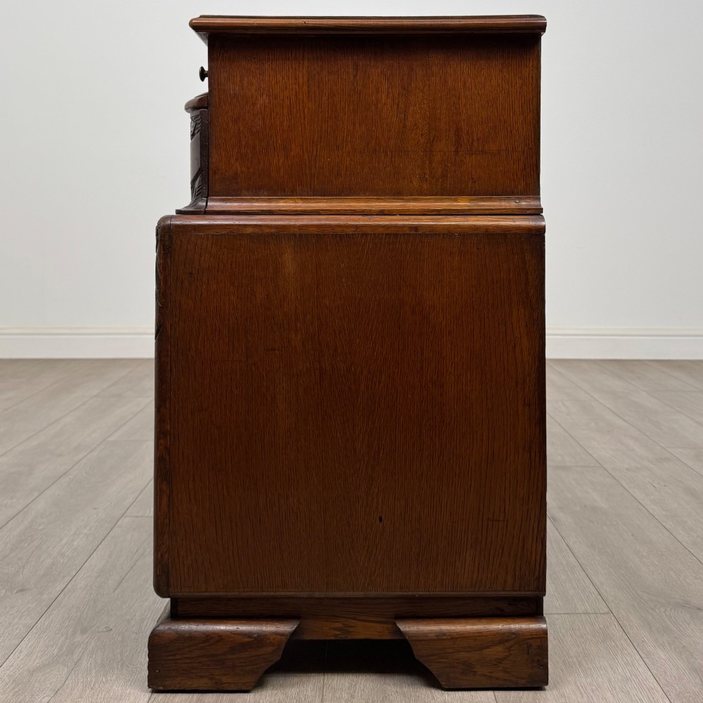 A dark carved oak chest of drawers featuring three drawers, floral relief carvings, and brass pendant handles set on carved bracket feet. View III
