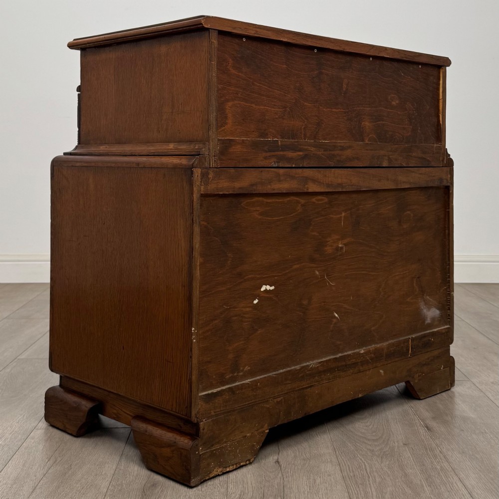 A dark carved oak chest of drawers featuring three drawers, floral relief carvings, and brass pendant handles set on carved bracket feet. View V