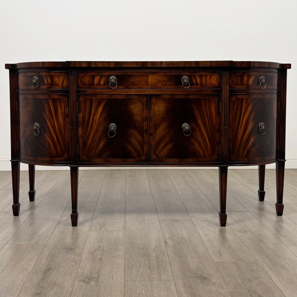 A 20th-century flame mahogany sideboard featuring a bow front design, drawers, cupboard doors, brass lion mask ring handles, and square tapered legs.