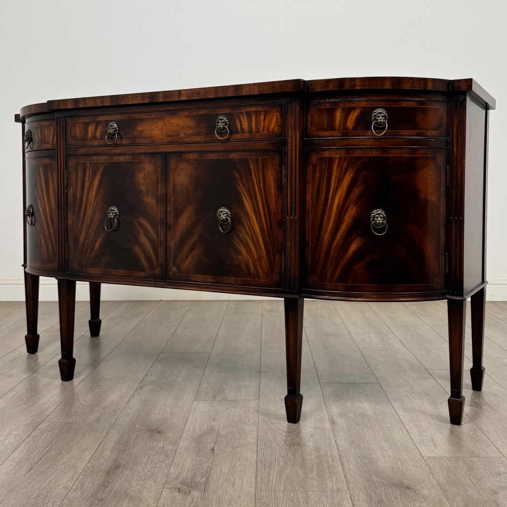 A 20th-century flame mahogany sideboard featuring a bow front design, drawers, cupboard doors, brass lion mask ring handles, and square tapered legs. View III