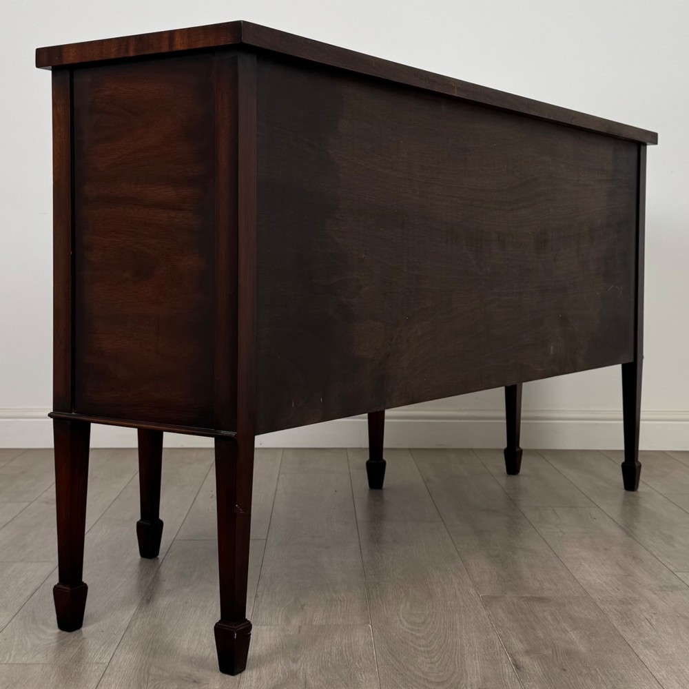 A 20th-century flame mahogany sideboard featuring a bow front design, drawers, cupboard doors, brass lion mask ring handles, and square tapered legs. View V