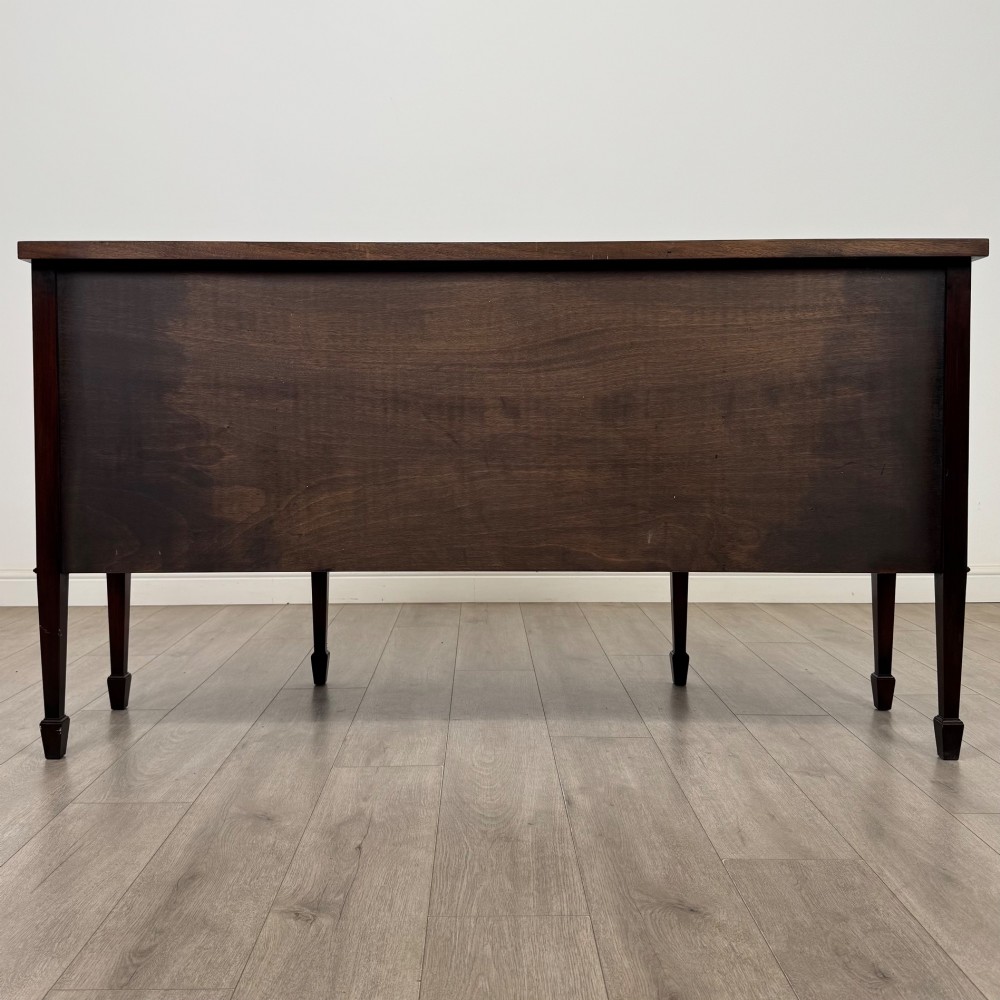 A 20th-century flame mahogany sideboard featuring a bow front design, drawers, cupboard doors, brass lion mask ring handles, and square tapered legs. View VI
