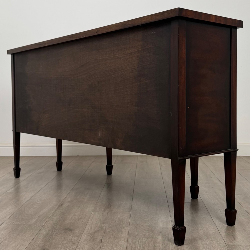 A 20th-century flame mahogany sideboard featuring a bow front design, drawers, cupboard doors, brass lion mask ring handles, and square tapered legs. View VII
