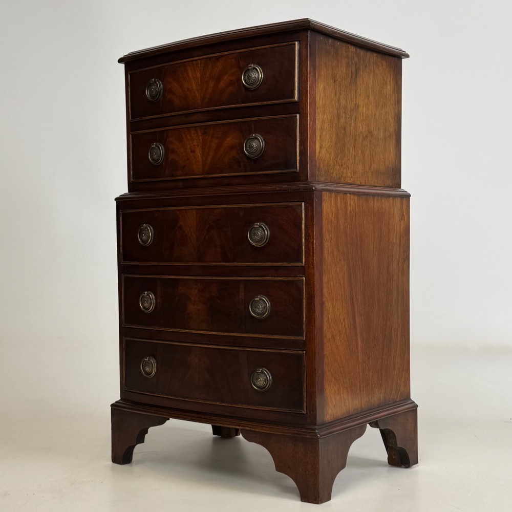 A small dark mahogany chest of drawers with five stacked drawers, brass ring handles, and bracket feet. View II