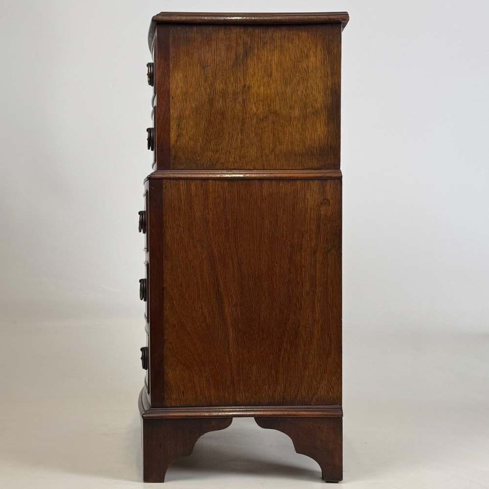 A small dark mahogany chest of drawers with five stacked drawers, brass ring handles, and bracket feet. View III