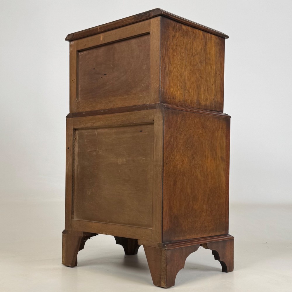 A small dark mahogany chest of drawers with five stacked drawers, brass ring handles, and bracket feet. View VI