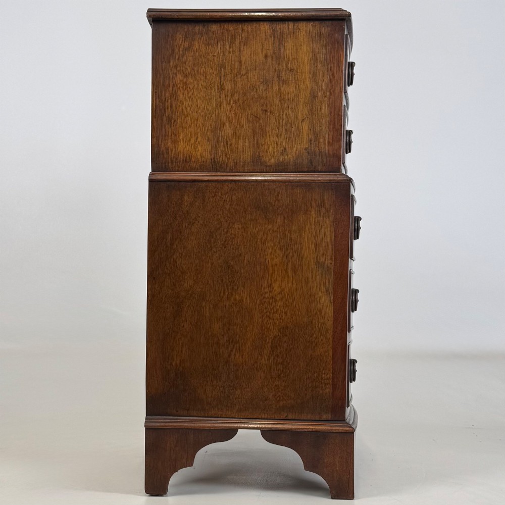 A small dark mahogany chest of drawers with five stacked drawers, brass ring handles, and bracket feet. View VII