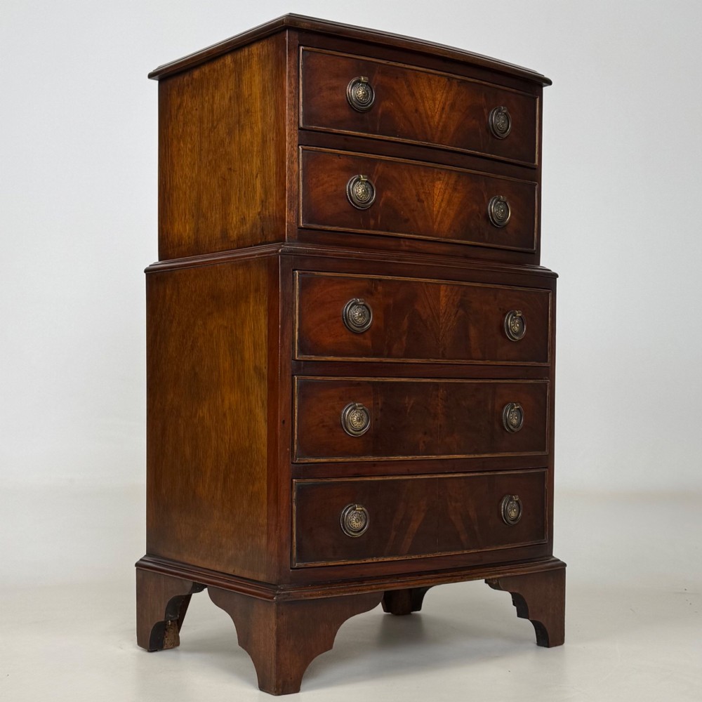 A small dark mahogany chest of drawers with five stacked drawers, brass ring handles, and bracket feet. View VIII