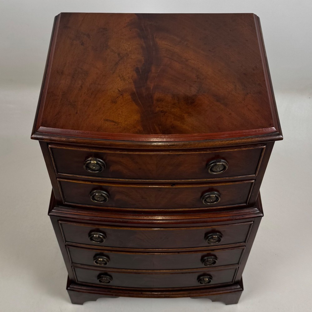 A small dark mahogany chest of drawers with five stacked drawers, brass ring handles, and bracket feet. View IX
