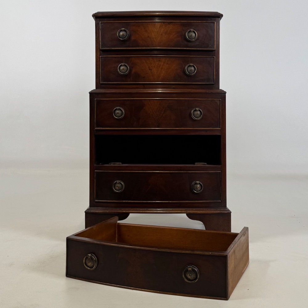 A small dark mahogany chest of drawers with five stacked drawers, brass ring handles, and bracket feet. View X