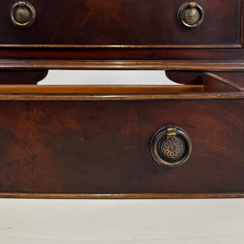 A small dark mahogany chest of drawers with five stacked drawers, brass ring handles, and bracket feet. View XI