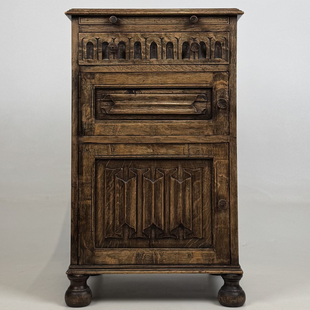 A small Edwardian carved dark oak cabinet with a single top drawer, a lower cupboard door, turned wooden knobs, and bun feet.
