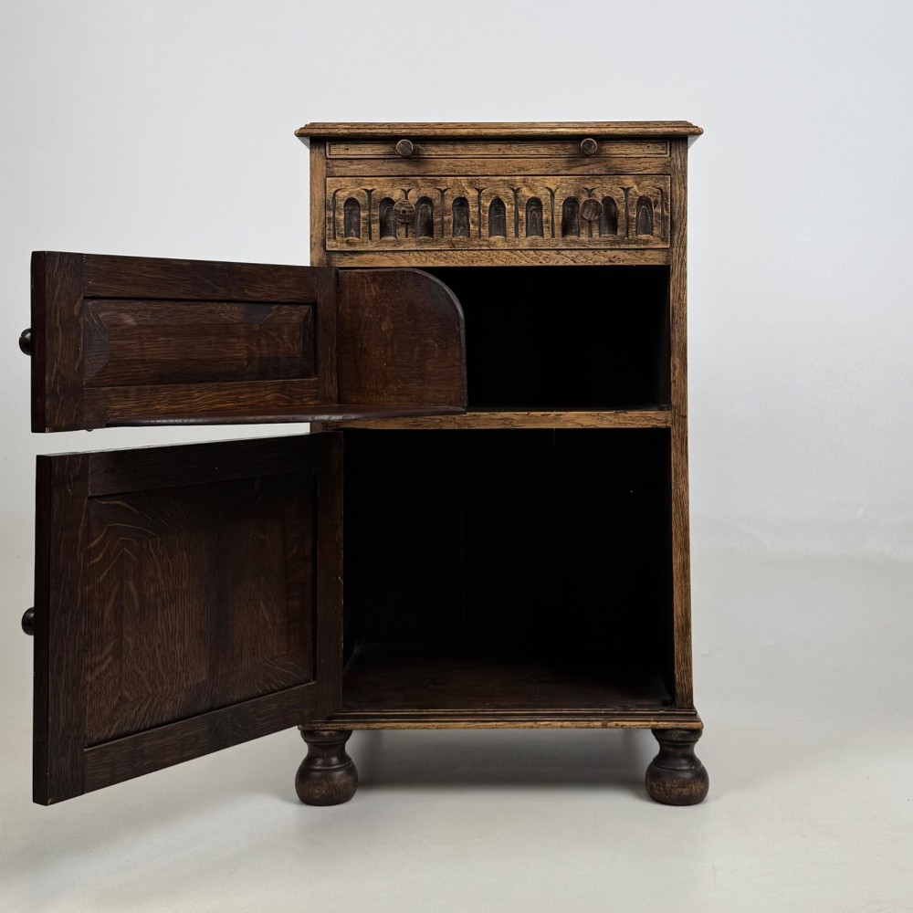 A small Edwardian carved dark oak cabinet with a single top drawer, a lower cupboard door, turned wooden knobs, and bun feet. View II