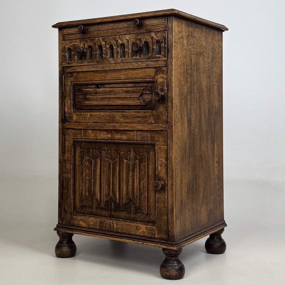 A small Edwardian carved dark oak cabinet with a single top drawer, a lower cupboard door, turned wooden knobs, and bun feet. View III