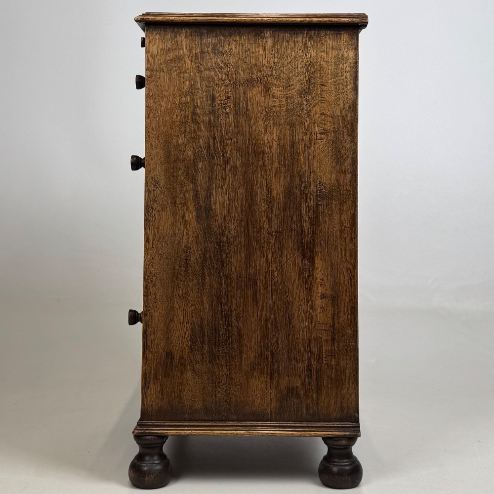 A small Edwardian carved dark oak cabinet with a single top drawer, a lower cupboard door, turned wooden knobs, and bun feet. View IV