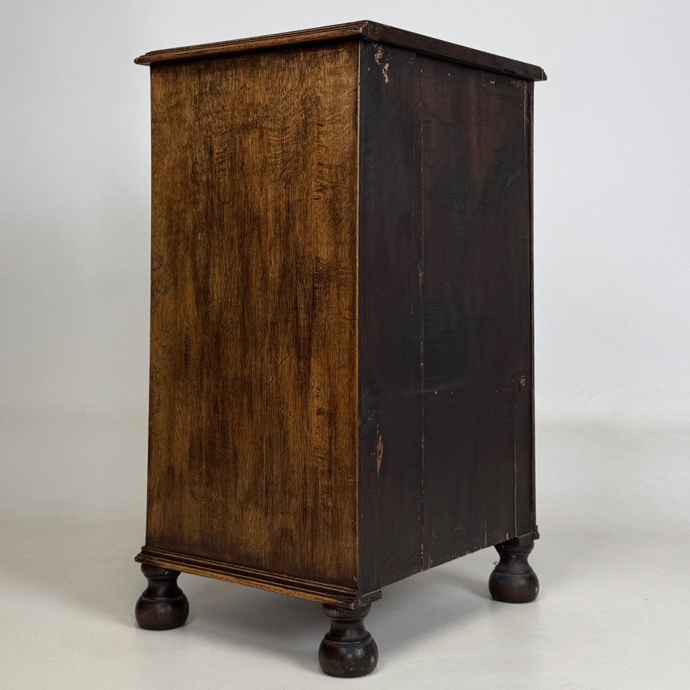 A small Edwardian carved dark oak cabinet with a single top drawer, a lower cupboard door, turned wooden knobs, and bun feet. View V