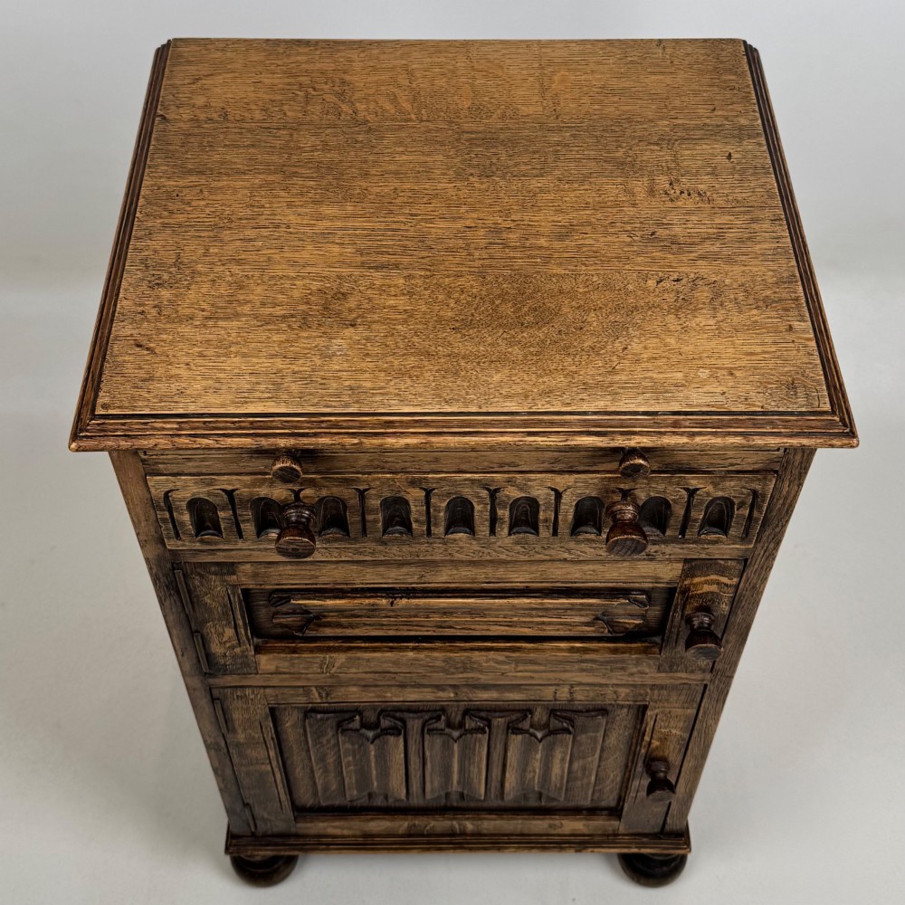 A small Edwardian carved dark oak cabinet with a single top drawer, a lower cupboard door, turned wooden knobs, and bun feet. View X